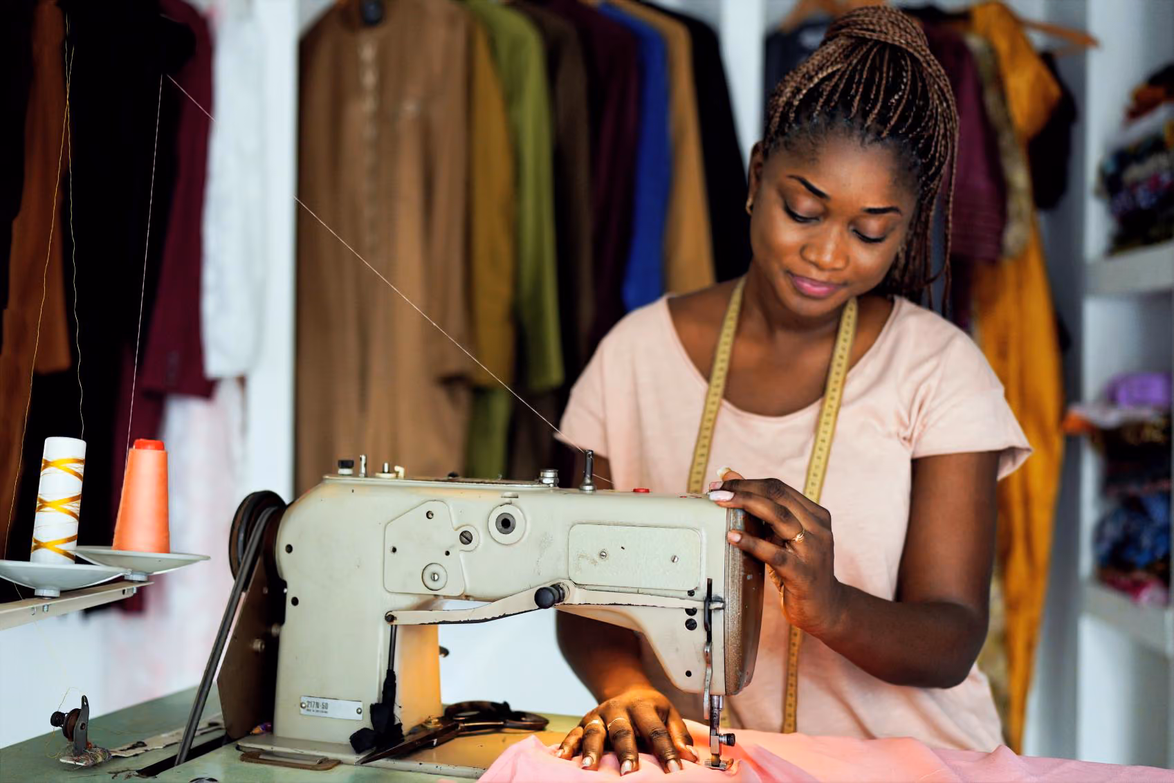 Orange Pro Mayotte Programme Entreprendre Femme souriante cousant un tissu rose avec une machine à coudre industrielle dans un atelier de couture.